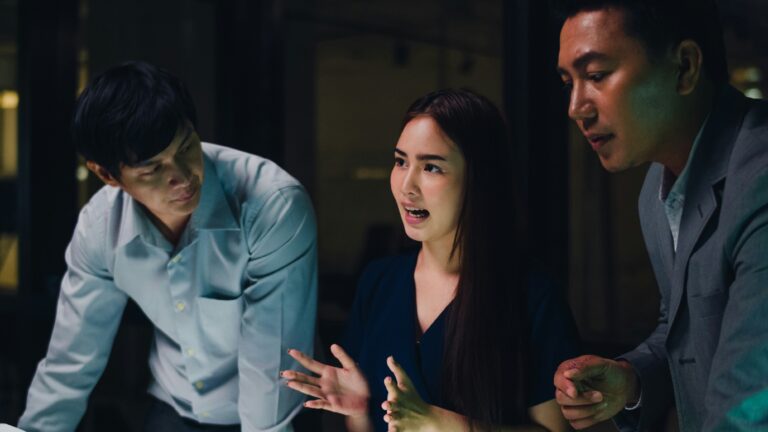 Three colleagues in discussion around a table in a darkened office at night